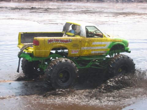 1992 Ford Bronco - Monster truck with custom paint and large tires navigates through a muddy terrain.