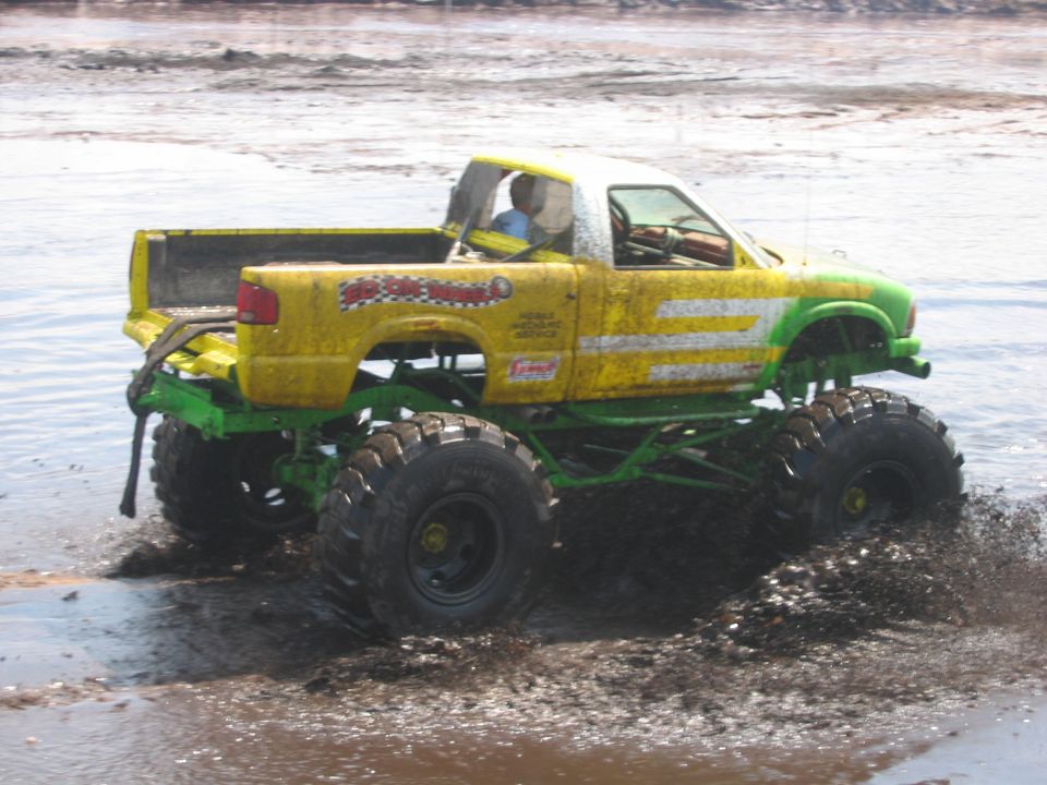 Yellow and green monster truck with large tires driving through mud. Text on door reads 'Super Swappers'