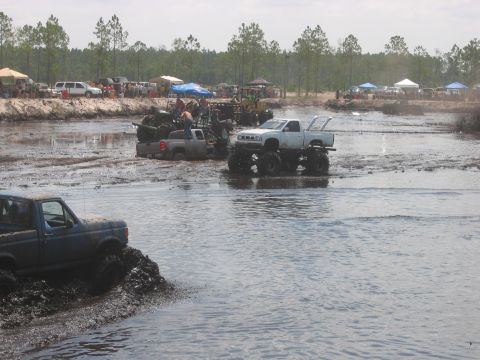 1992 Ford Bronco - Multiple modified trucks navigate a muddy track during an off-road event.