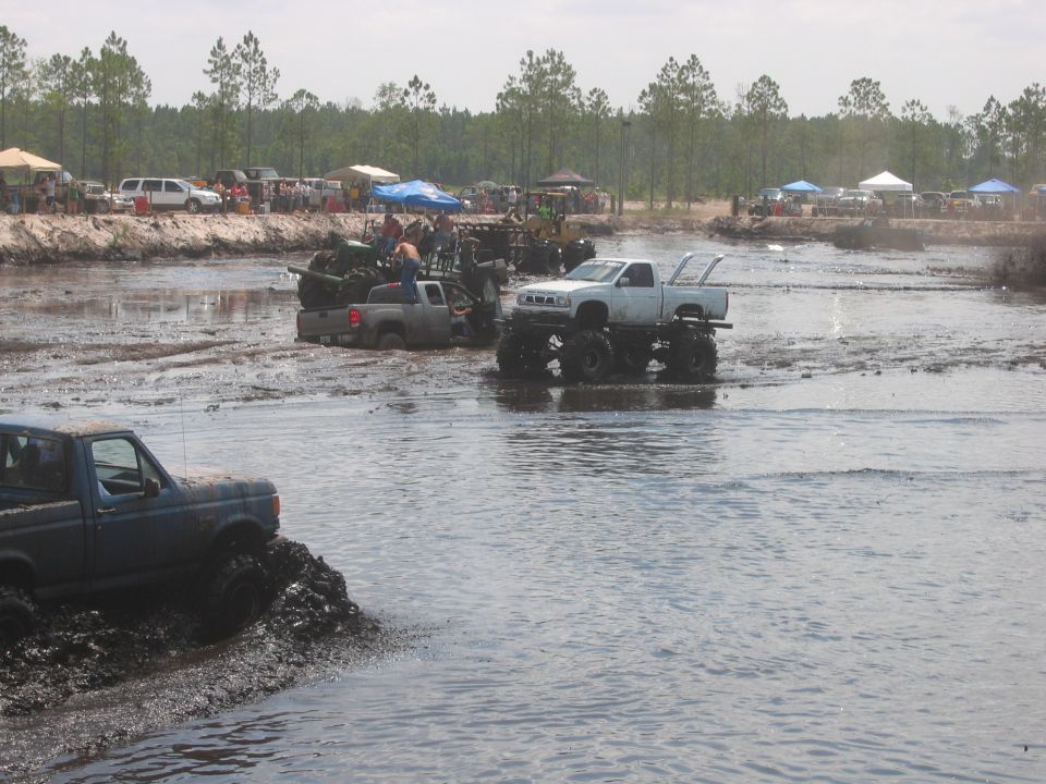 Trucks driving through a mud pit with spectators on the bank