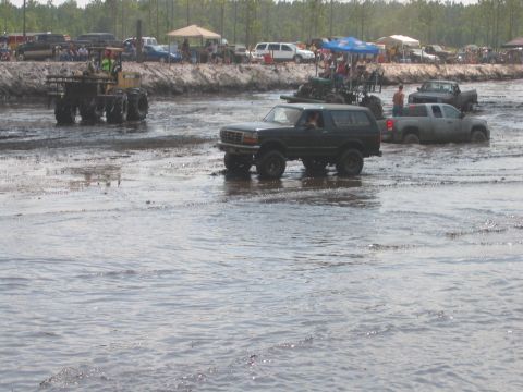 1992 Ford Bronco - A 1992 Ford Bronco navigates a muddy track with other vehicles in the background.