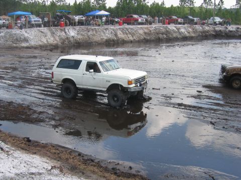 1992 Ford Bronco - A white Ford Bronco navigates a muddy track with other vehicles in the background.