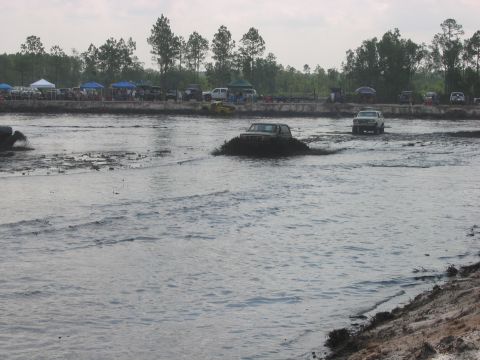 1992 Ford Bronco - A Jeep Cherokee XJ navigates a mud pit while another SUV follows in the background at an off-road event.