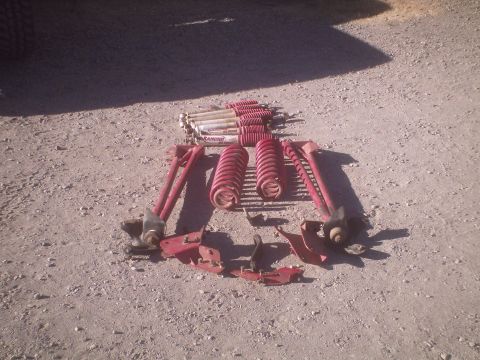 1991 Ford Bronco - A collection of red suspension components, including Rancho shocks and coil springs, are displayed on a gravel surface.