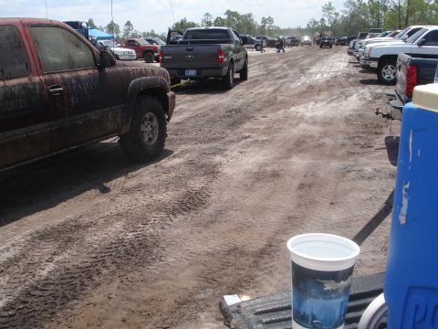 1989 Ford Bronco - Several trucks are parked on a muddy, tire-tracked dirt road under a partly cloudy sky.
