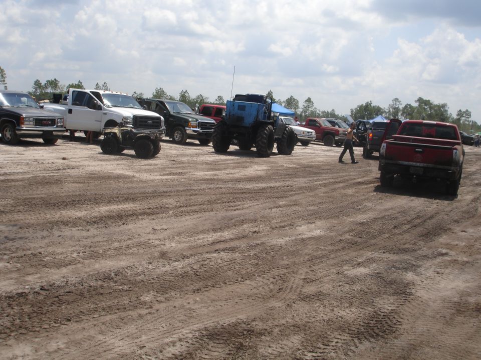 Muddy field with several trucks and a large blue tractor, one person walking