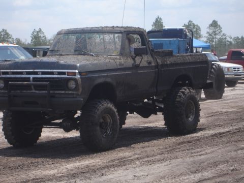1989 Ford Bronco - Muddy 1970s Ford pickup truck on a dirt track with another vehicle in the background.