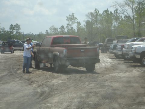 1989 Ford Bronco - Several trucks are parked in a dusty lot under a cloudy sky.