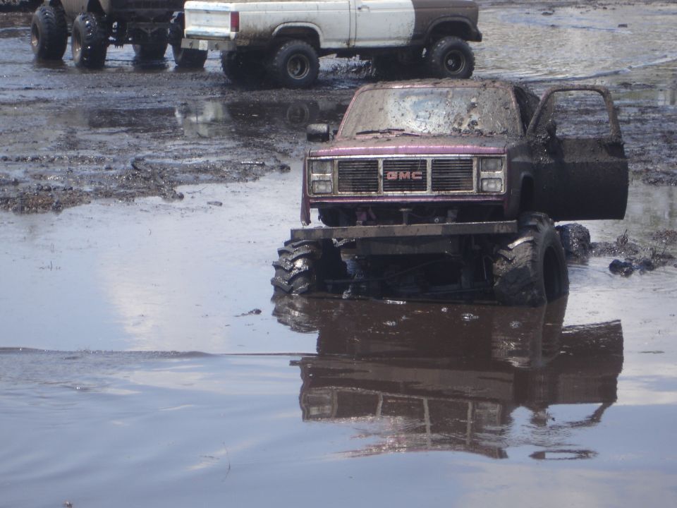 Mud-covered GMC pickup truck with open driver's door, front view, in shallow water