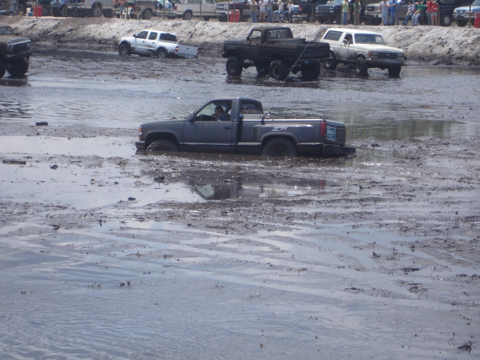 Dark gray pickup truck stuck in mud, side view. Other vehicles visible in background