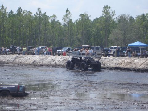 1989 Ford Bronco - A custom-built monster truck navigates a muddy track while spectators watch from the sidelines.