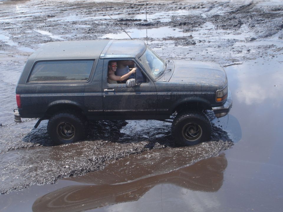 Dark gray 1989 Ford Bronco driving through mud, driver visible
