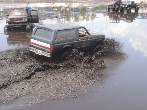 1989 Ford Bronco - A 1989 Ford Bronco navigates a muddy obstacle course, kicking up water and dirt.