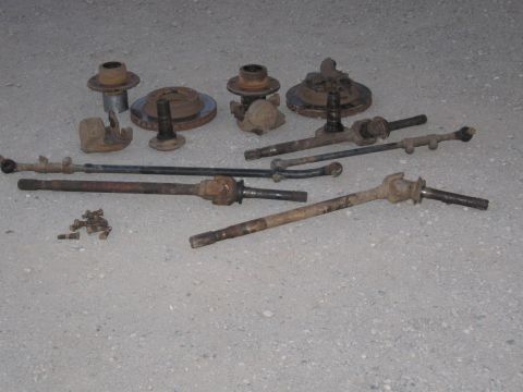 1991 Ford Bronco - Various used vehicle parts, including axle shafts and steering linkages, are displayed on the ground.