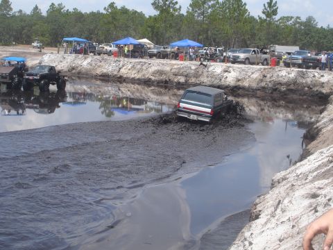 1989 Ford Bronco - A dark SUV, identified as a 1989 Ford Bronco, navigates a muddy track during an off-road event.