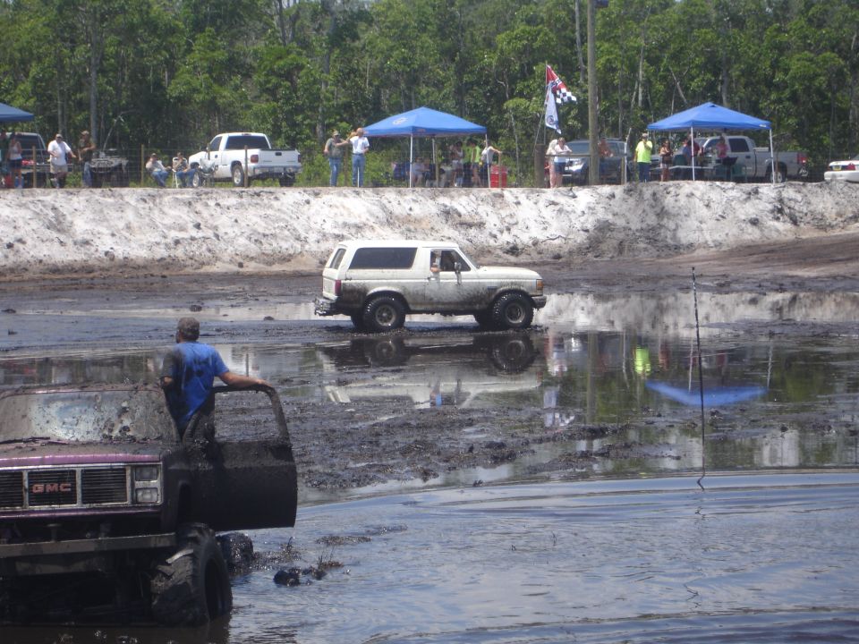 1989 Ford Bronco driving through a mud pit with spectators in the background