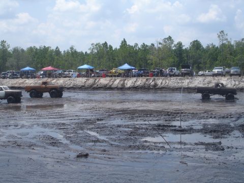 1989 Ford Bronco - Several trucks are stuck in a mud pit during an event, with people watching from the bank.