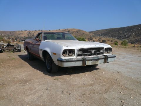 1975 Ford Ranchero - A 1975 Ford Ranchero sits in a dry, outdoor lot, its front end notably altered and missing headlights.