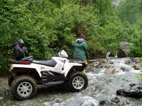 2000 Ford E350 - An all-terrain vehicle navigates a rocky stream surrounded by dense foliage.