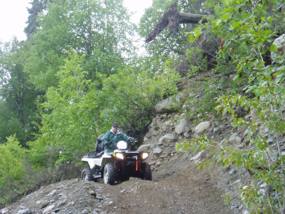 White all-terrain vehicle with a rider on a rocky, wooded trail
