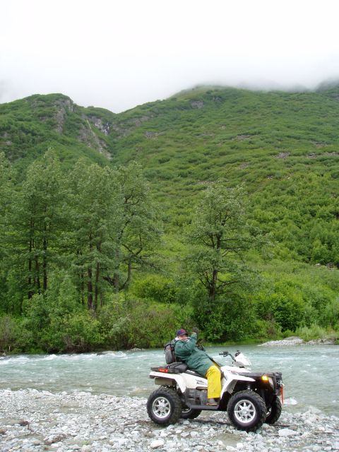 2000 Ford E350 - A person rides an all-terrain vehicle (ATV) on a rocky shore next to a river. The ATV is white with silver rims and the rider is wearing a…