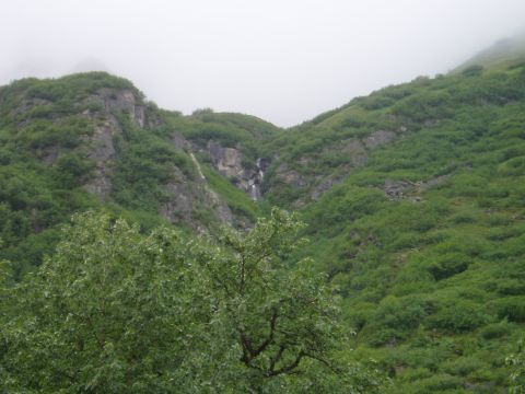 2000 Ford E350 - A misty, overcast day shows a lush green mountainside with a thin waterfall cascading down a rocky crevice. Trees and foliage cover the slo…