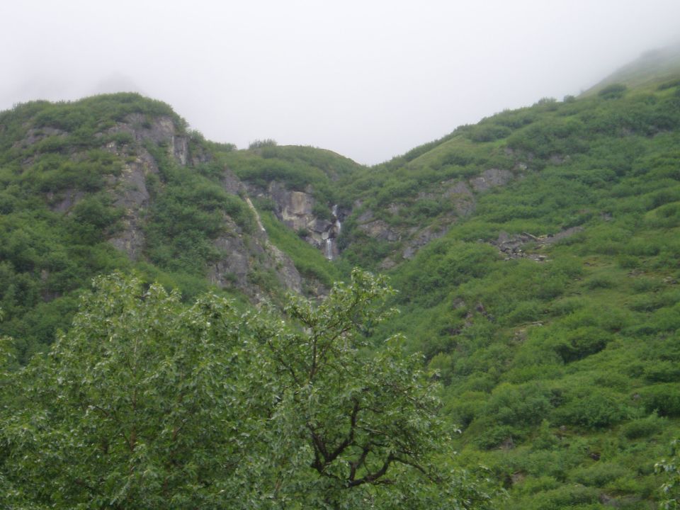 Misty mountain landscape with a waterfall and dense green foliage.