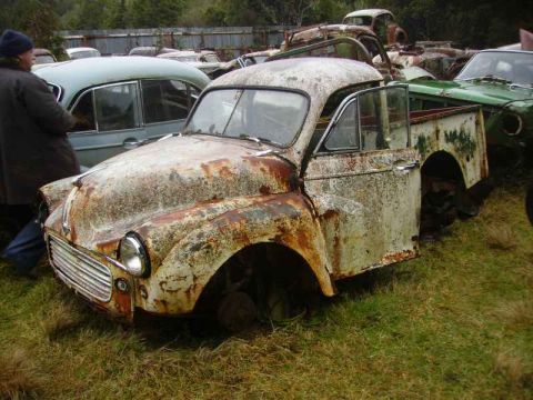 1969 MINI Cooper - Junkyard scene with a heavily rusted pickup truck in the foreground and other vehicles in the background.
