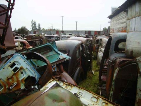 1969 MINI Cooper - A collection of vintage vehicles and parts are piled up in a junkyard under an overcast sky.