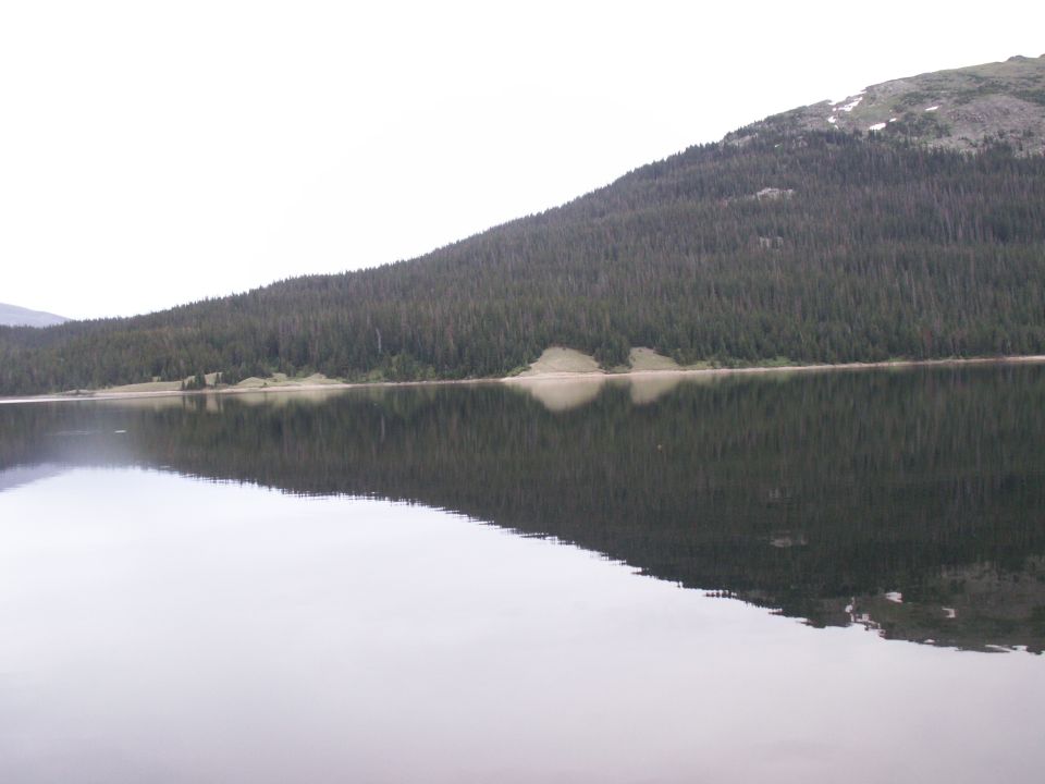 Calm lake reflecting a dense forest on a hillside.