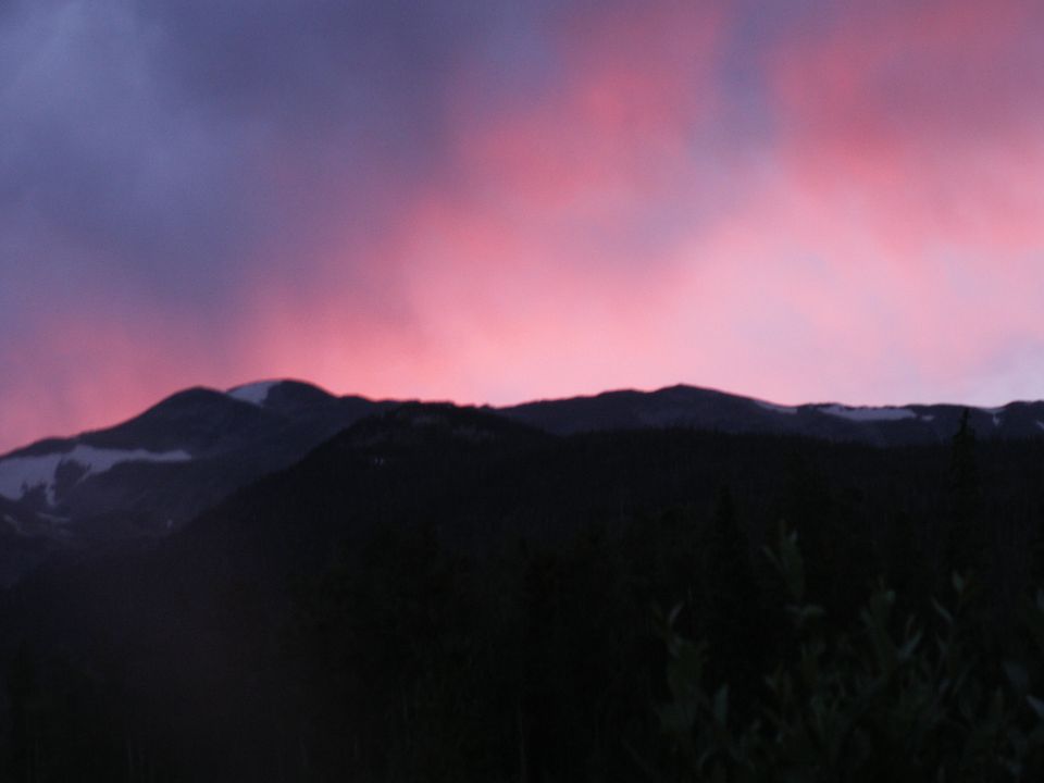 Sunset sky with pink and purple clouds over dark mountains and forest.