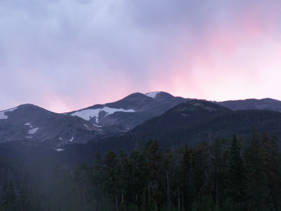 Mountain range with snow-capped peaks under a dusky sky with pink and purple light.