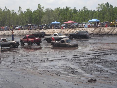 1989 Ford Bronco - A dark colored SUV is driving through a muddy track with other trucks and SUVs in the background. The vehicle is partially submerged in the…