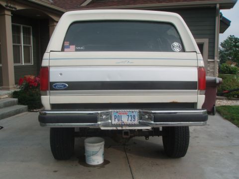 1987 Ford Bronco - The rear view of a white Ford Bronco with a camper shell is shown parked on a concrete driveway. Visible details include the license plate…