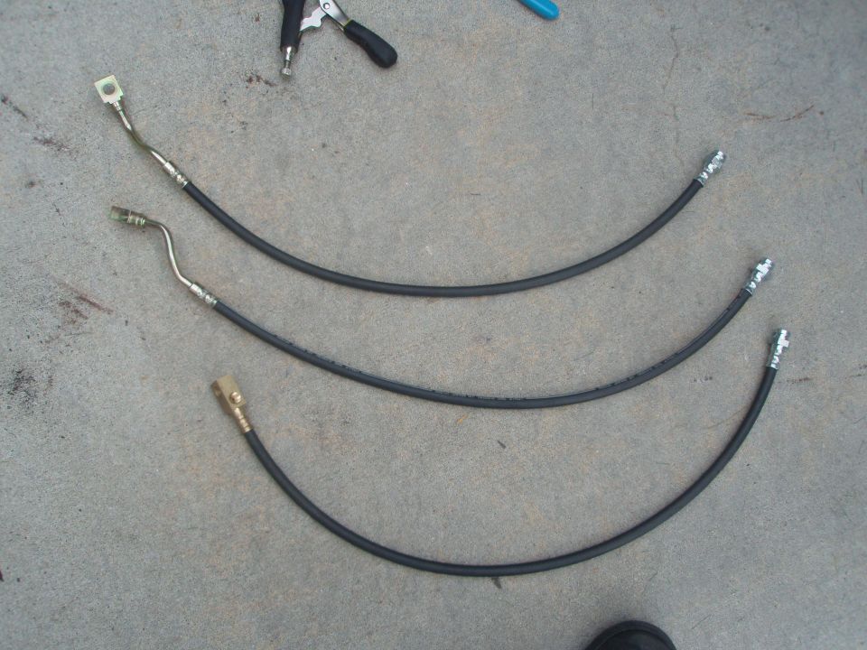 Three black rubber brake hoses with metal fittings on concrete.