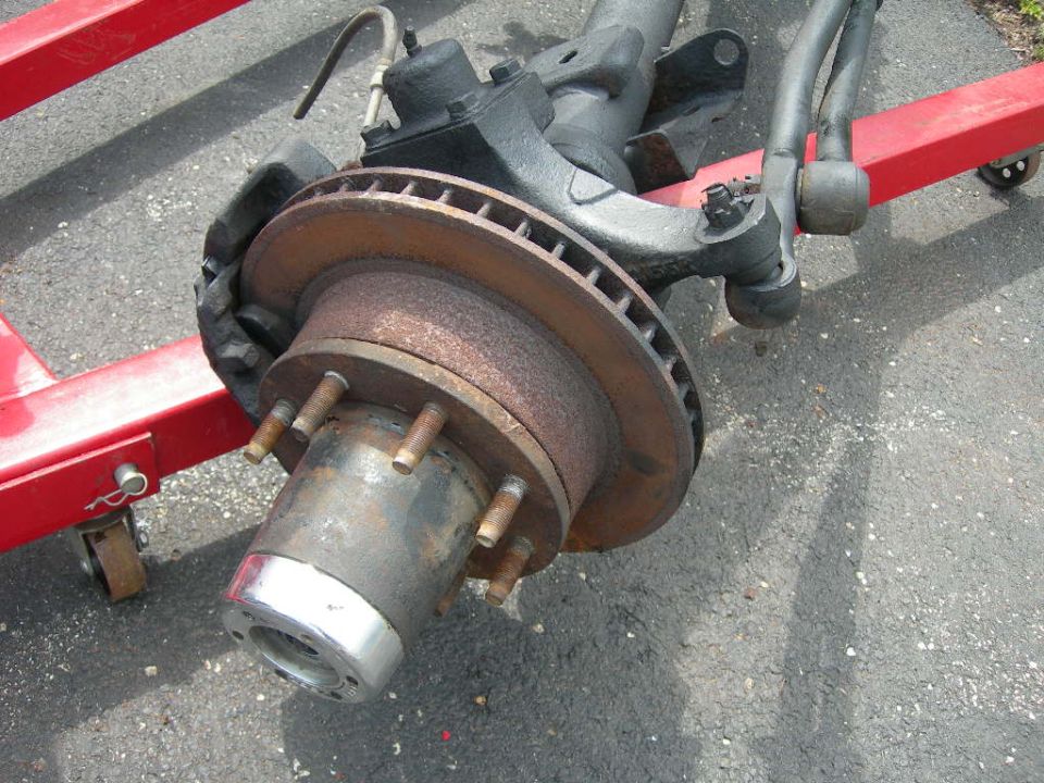 Vehicle front axle assembly with brake rotor and hub on red engine hoist.