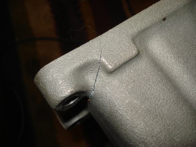Close-up of cracked gray textured plastic part corner near a bolt hole