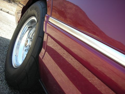 1992 Ford Crown Victoria - A close-up, low-angle shot shows the driver's side rear wheel and fender of a dark red vehicle. The tire is a Mickey Thompson drag radial,…