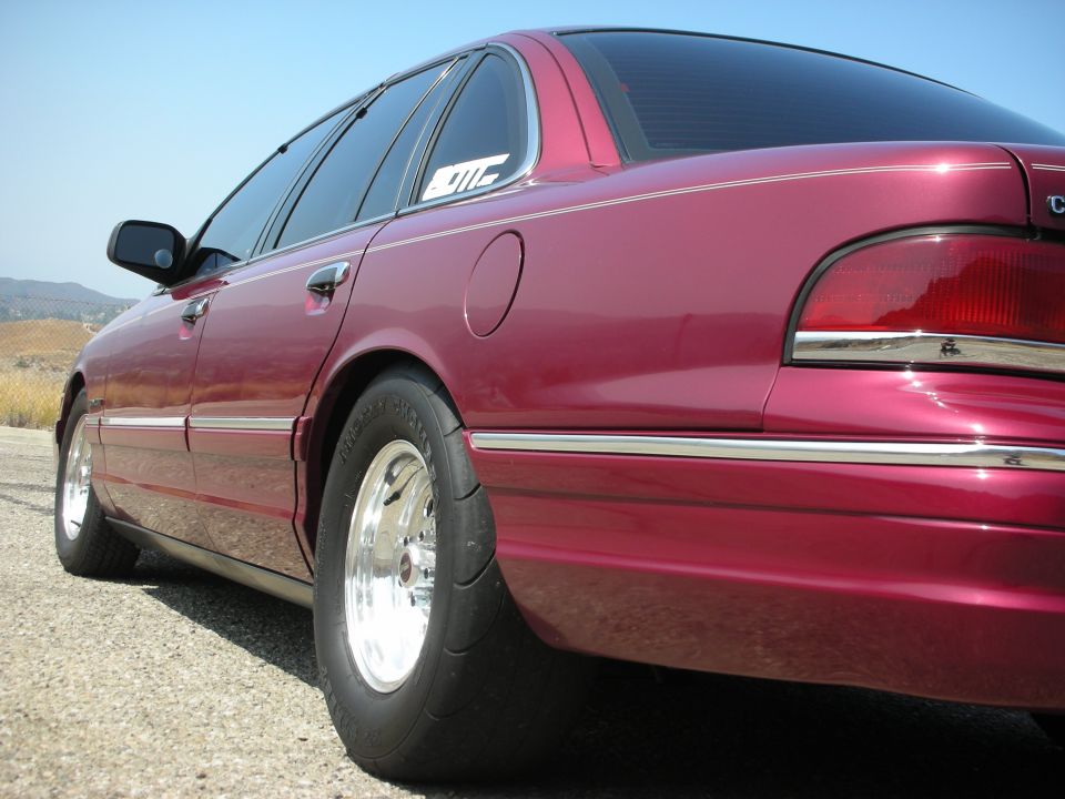 Maroon sedan with drag tires, chrome wheels, and a sticker on the rear window.