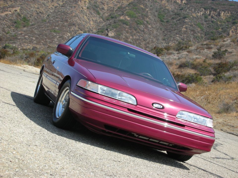 Maroon 1992 Ford Crown Victoria parked on a road with hills behind it.