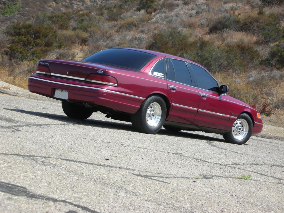 Maroon Ford Crown Victoria with tinted windows and chrome wheels parked on a road.