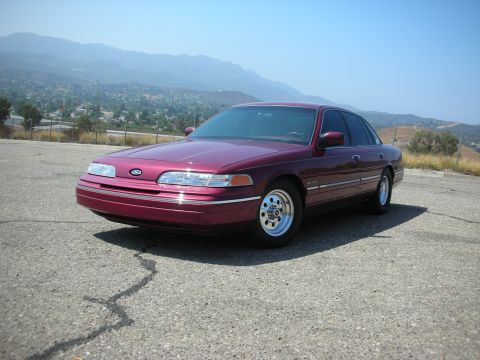 1992 Ford Crown Victoria - A maroon 1992 Ford Crown Victoria is parked on a cracked asphalt surface with a mountainous landscape in the background.