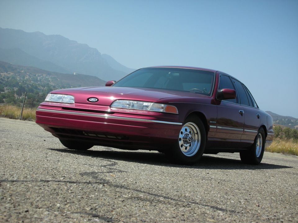 Maroon 1992 Ford Crown Victoria sedan parked on asphalt road, hills in background.