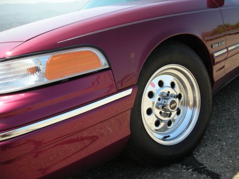 1992 Ford Crown Victoria - Close-up of the front passenger side of a maroon Ford Crown Victoria, showing the headlight, fender, and a chrome Weld racing wheel with a…