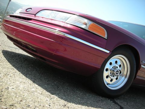 1992 Ford Crown Victoria - Low angle shot of the front passenger side of a dark red 1990s Ford Crown Victoria. The car features a chrome wheel with a polished lip and…