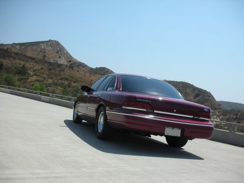 1992 Ford Crown Victoria - The rear passenger side of a dark red 1992 Ford Crown Victoria LX is shown parked on a concrete surface with a mountainous, dry landscape i…
