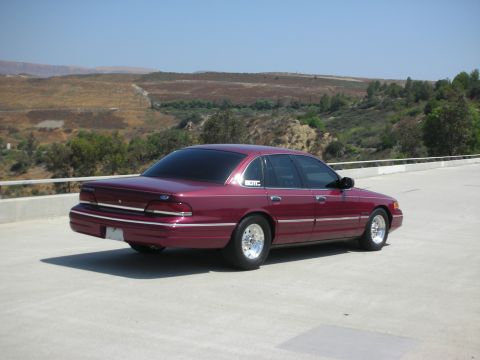 1992 Ford Crown Victoria - A maroon 1992 Ford Crown Victoria is parked on a concrete surface with a hilly, dry landscape in the background.