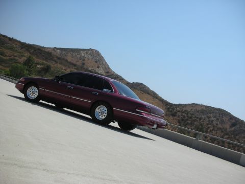 1992 Ford Crown Victoria - A maroon 1992 Ford Crown Victoria is parked on a concrete incline with a mountainous, arid landscape in the background under a clear blue s…