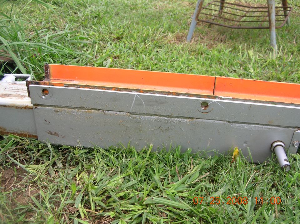Close-up of a metal machine part with an orange top surface on grass.