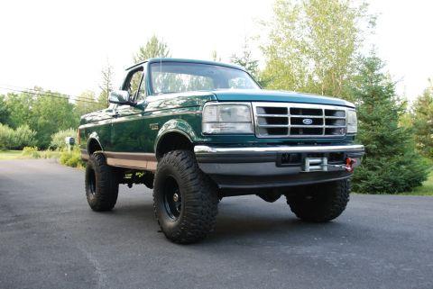 1996 Ford Bronco - Photograph of a green lifted Ford Bronco parked in a driveway, not a document.